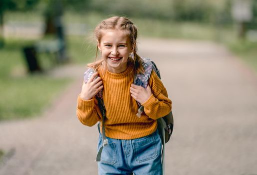 Pretty school girl with backpack looking at camera and smiling. Carefree child kid at autumn outdoors portrait