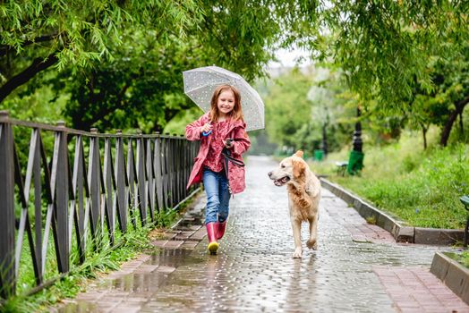 Little girl walking under rain with umbrella and golden retriever dog, panoramic orientation