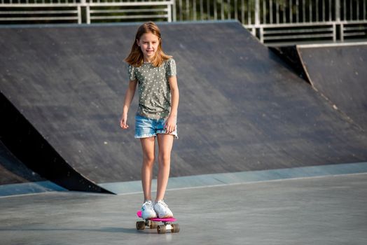 Preteen girl riding on skateboard at park ramp in summertime. Beautiful female child skater with board outdoors practicing