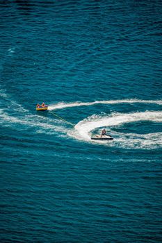 Inflatable attraction. Happy people are going to swim on an air mattress behind a jet ski. Tourists ride the inflatable watercraft boat. Jet ski skating people on a large Inflatable raft