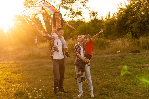 Happy family with a kite playing at sunset in the field