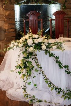 The presidium of the newlyweds in the banquet hall of the restaurant is decorated with candles and green plants, wisteria hangs from the ceiling