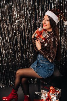 a girl in a shiny jacket with a Santa hat with gifts on a silver background in the form of rain.