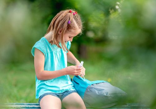 School girl with sanitizer sitting on bench in park