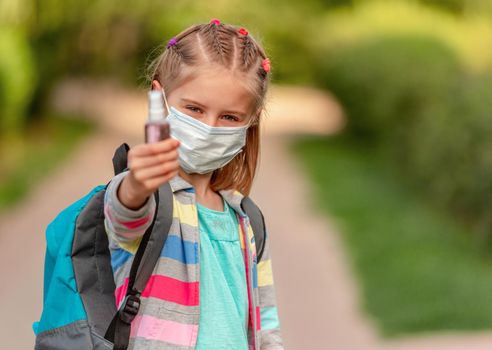 Portrait of school girl in mask holding sanitizer on nature background