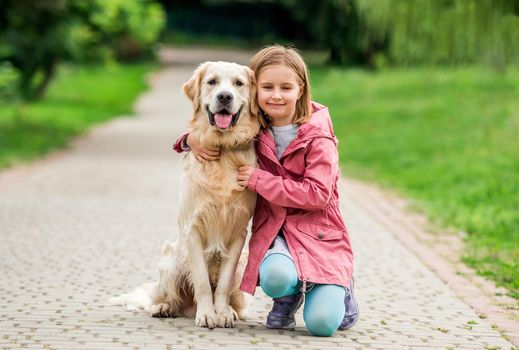 Little girl walking with golden retriever in green park