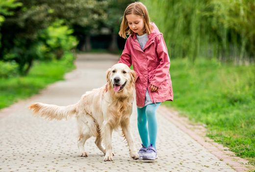 Little girl walking with golden retriever outdoors in park