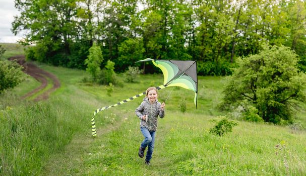 Happy little girl flying bright kite outdoors on nature in spring