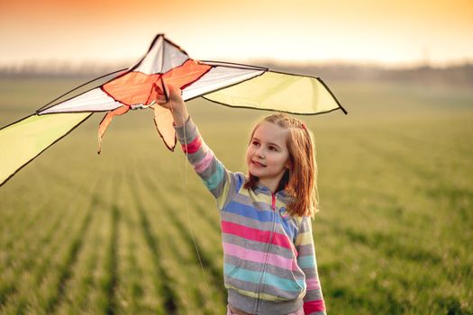 Beautiful little girl with flying kite on sunny field