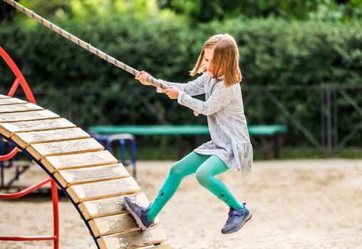 Child climbing with rope on sport playground outdoors at sunny day