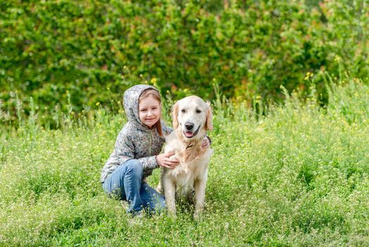 Happy little girl hugging cute dog on blooming meadow