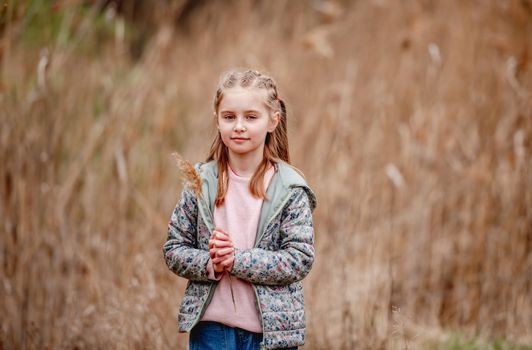 Portrait of little girl standing and holding spikelet in her hands on the nature in spring time
