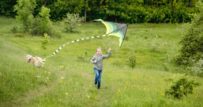 Happy little girl flying bright kite outdoors on nature in spring