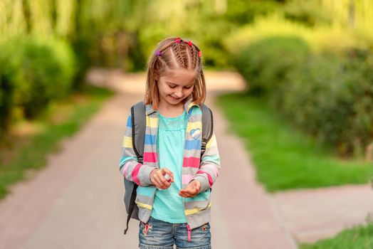 Little girl using hand sanitizer after school in park