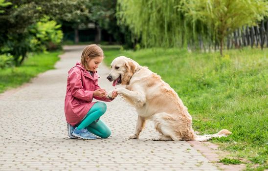 Golden retriever giving paw to little girl sitting on park road