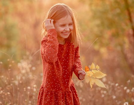 Happy little girl walking outdoors with yellow leaves in hand