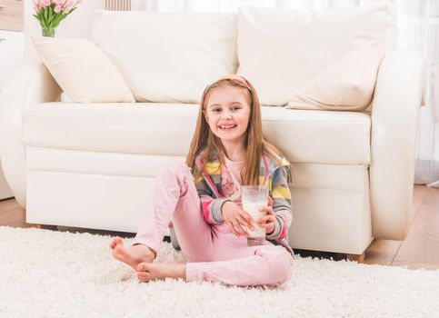 Smiling little girl sitting in front of a couch with glass of milk