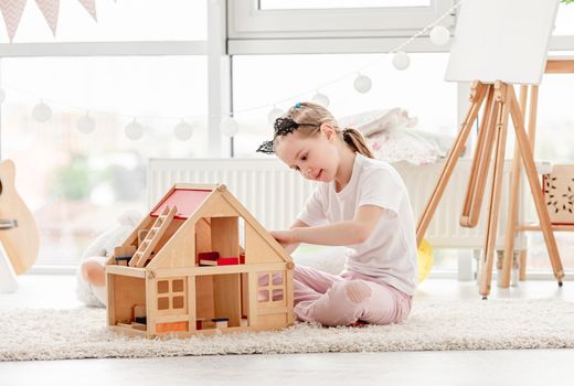 Pretty little girl plays with wooden dollhouse in children's room
