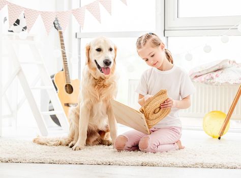 Cute little girl and adorable dog reading book in children's room