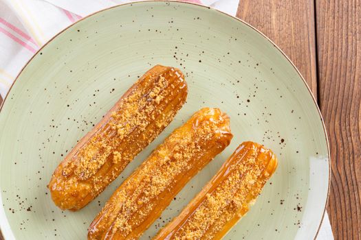 Three eclaies with nuts topping on green plate close up