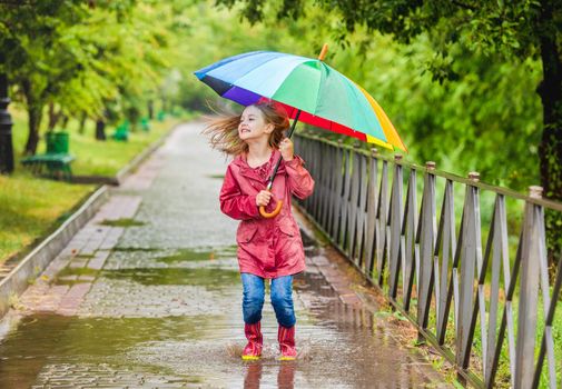 Little girl with umbrella jumping in puddle during rainy walk in park