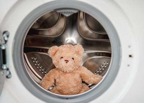 Plush teddy bear after washing in machine sitting inside with open door