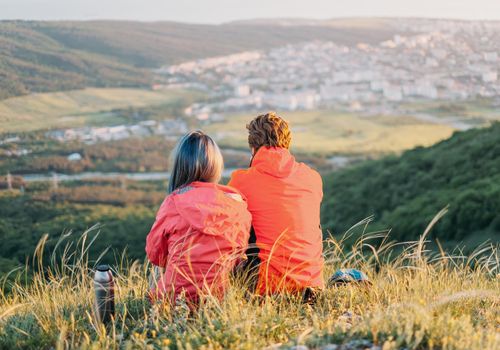 Traveler loving couple sitting on mountain meadow and looking into the distance in summer, rear view.