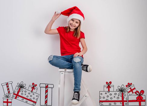 Smiling little girl in santa hat sitting beside christmas presents sketch drawn on white wall background