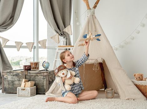 Happy little girl flying wooden plane sitting in room with retro things