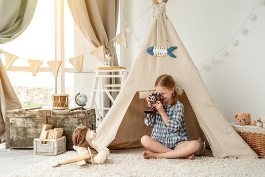 Cute little photographer shooting plush teddy in pilot hat at home