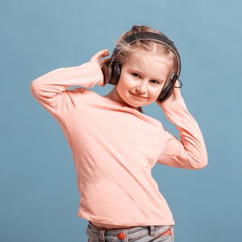 Cute little girl with headphones listening to music on light blue background. Copyspace