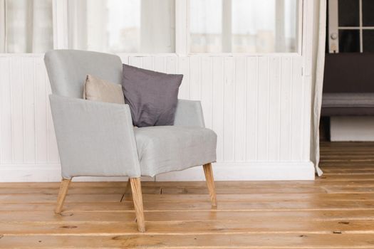 Interior shot of simple comfortable armchair with cushions on wooden floor