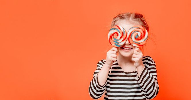 Cute kid girl holding two round colourful lollypops in front of her eyes