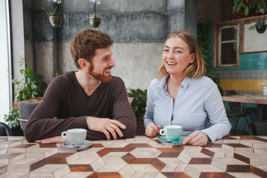 Cheerful young couple sitting on date in cafe and drinking coffee.
