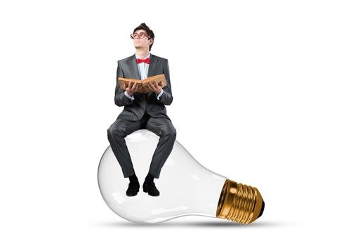Young businessman sits on an electric light bulb. holds a book in his hands