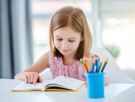 Little girl reading book at desk in classroom