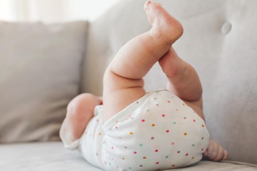 Unrecognizable baby in spotted clothing lying on soft sofa in stylish room