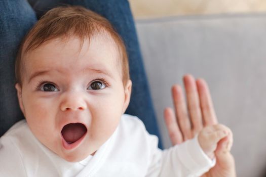 Cute baby looking at camera with surprised face expression and holding hand of mother