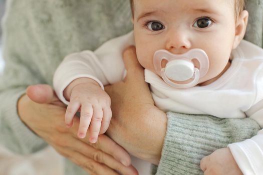 Anonymous mother in sweater holding and embracing adorable baby with pacifer