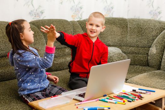 Two beautiful cute happy smiling children, a boy and a girl, use laptop for distance learning or entertainment.