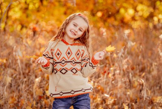 Cute little girl holding yellow leaves on blurred autumn background