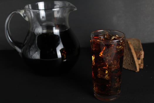 Dark bread kvass poured into a glass with solder and stands on a gray black background with a place for text and copyspace.