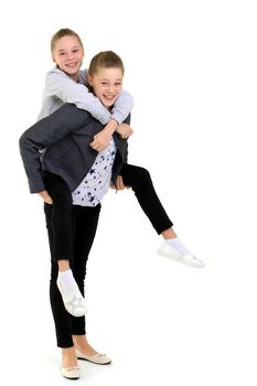 Happy Smiling Girl Piggy Backing her Twin Sister, Full Length Portrait of Two Cheerful Pretty Teenage Girls in Fashionable Stylish Outfit Having Fun Together Against White Background in Studio