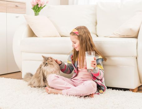 Little girl petting her cute cat and holding glass of milk