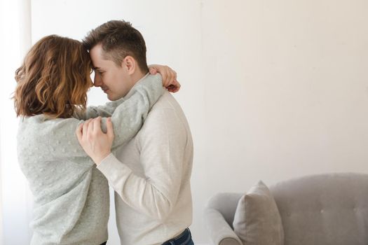 Side view of young loving couple standing and embracing at couch at home.