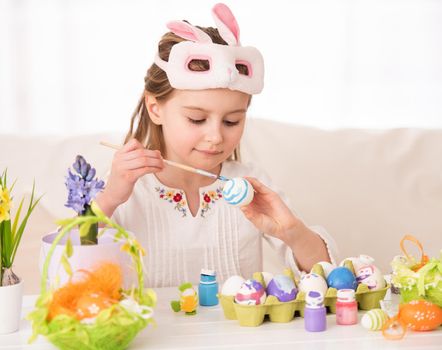Pretty girl coloring eggs for Easter in bunny mask