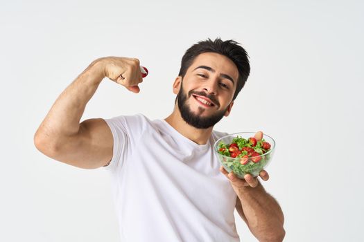 Cheerful man in a white T-shirt with a plate of light green and a healthy meal. High quality photo