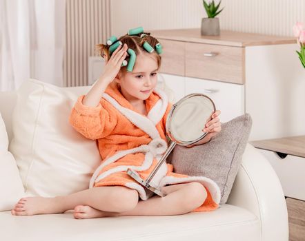 Pretty child girl with curlers looking in the mirror