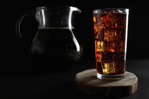 kvass drink in a dark low key kvass drink in an iced glass and a jug with a drink with room for text.