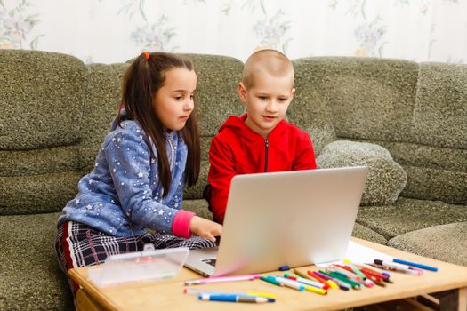 Two beautiful cute happy smiling children, a boy and a girl, use laptop for distance learning or entertainment.